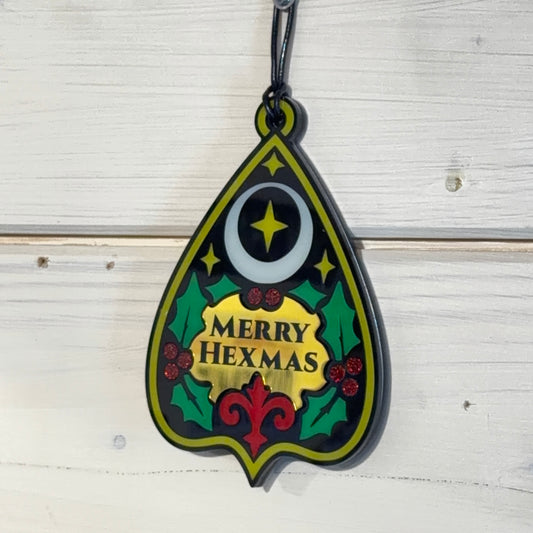 Merry Hexmas Ouija Planchette Ornament hanging on a white wood background