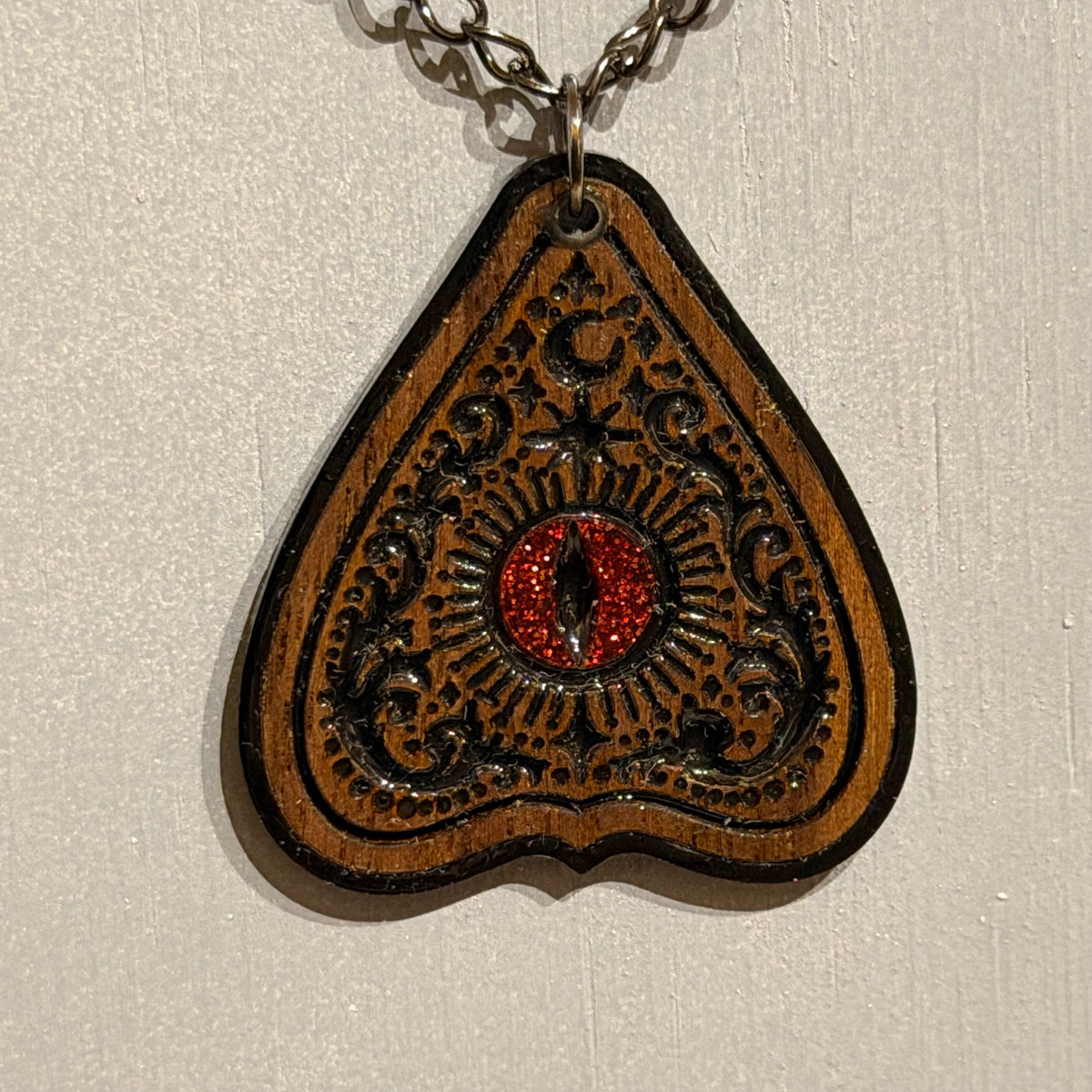 Ouija-inspired wooden planchette pendant with ornate black detail and glossy resin finish