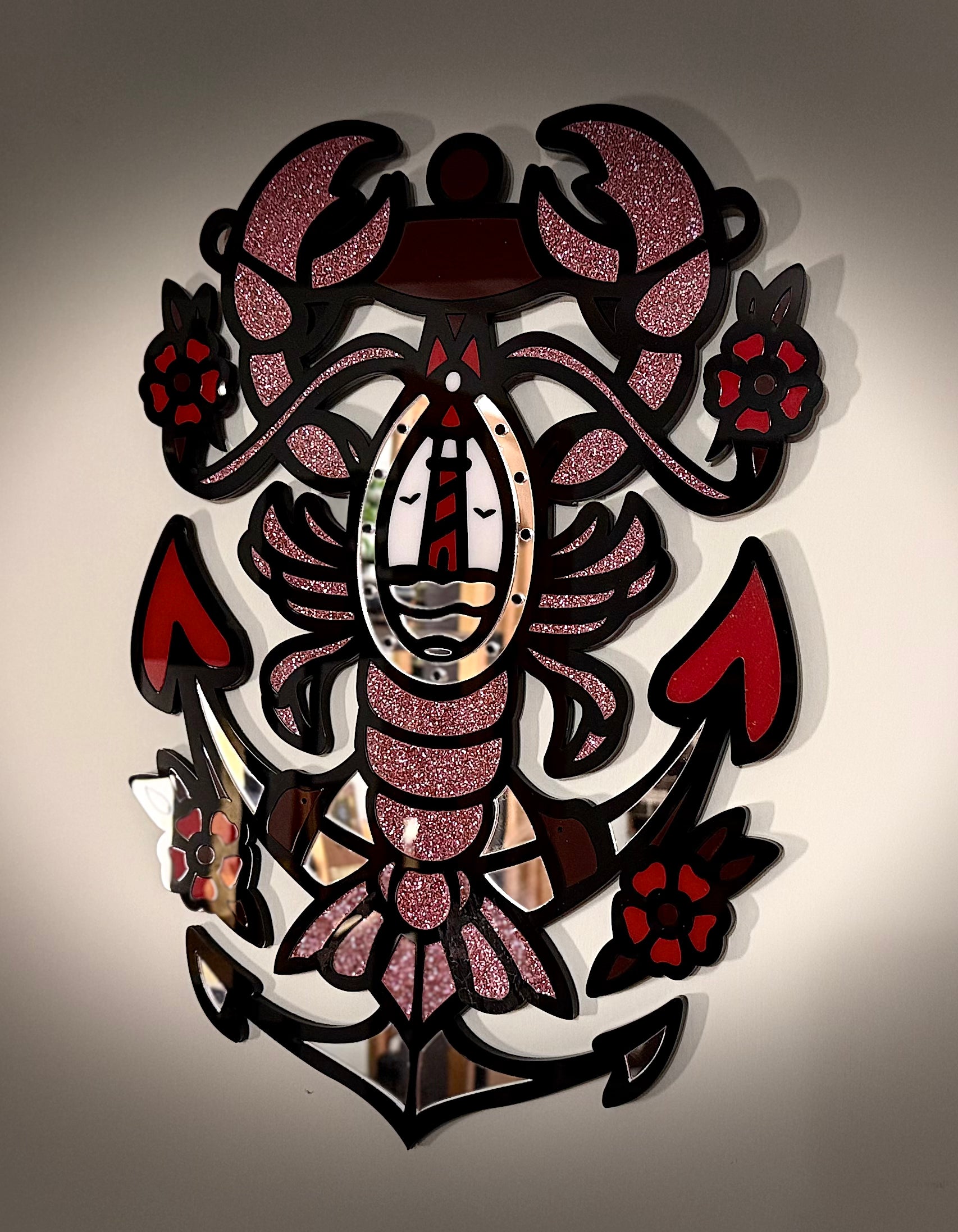 Front view of the Lobster & Anchor acrylic wall hanging showing a lobster embracing an anchor with a lighthouse at its core; glitter pink claws and floral accents.