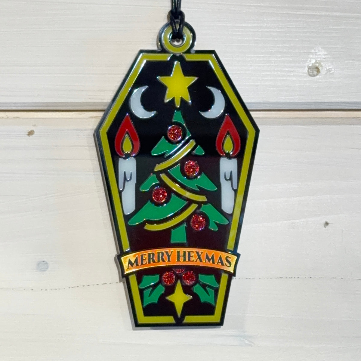 Front view of Merry Hexmas coffin ornament hanging against a white timber background
