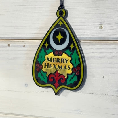 Merry Hexmas Ouija Planchette Ornament hanging against white wooden boards